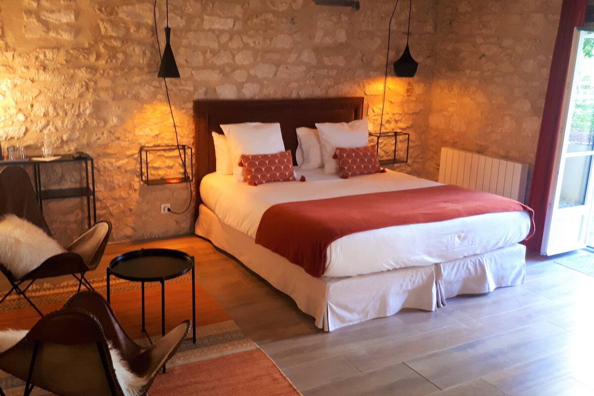 Un dormitorio con una cama grande, dos sillones, una mesita y una pared de piedra.