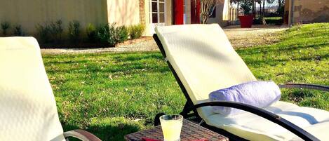Two lounge chairs with a glass of lemonade on a small table, set on a grassy lawn with a building in the background.