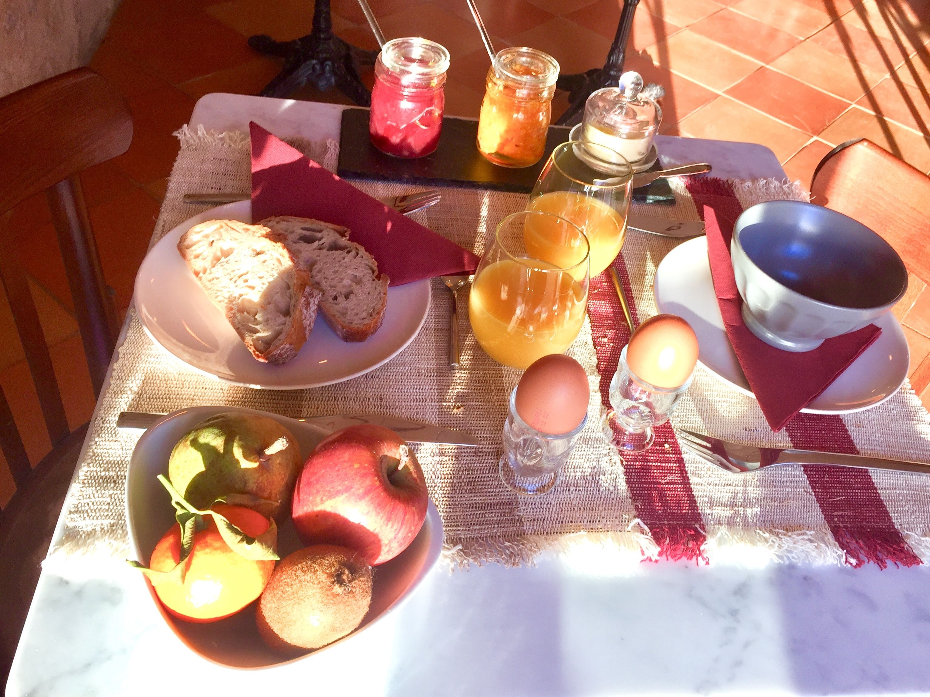 Una mesa de desayuno con pan, fruta, un vaso de jugo de naranja, una vela y un frasco de mermelada.