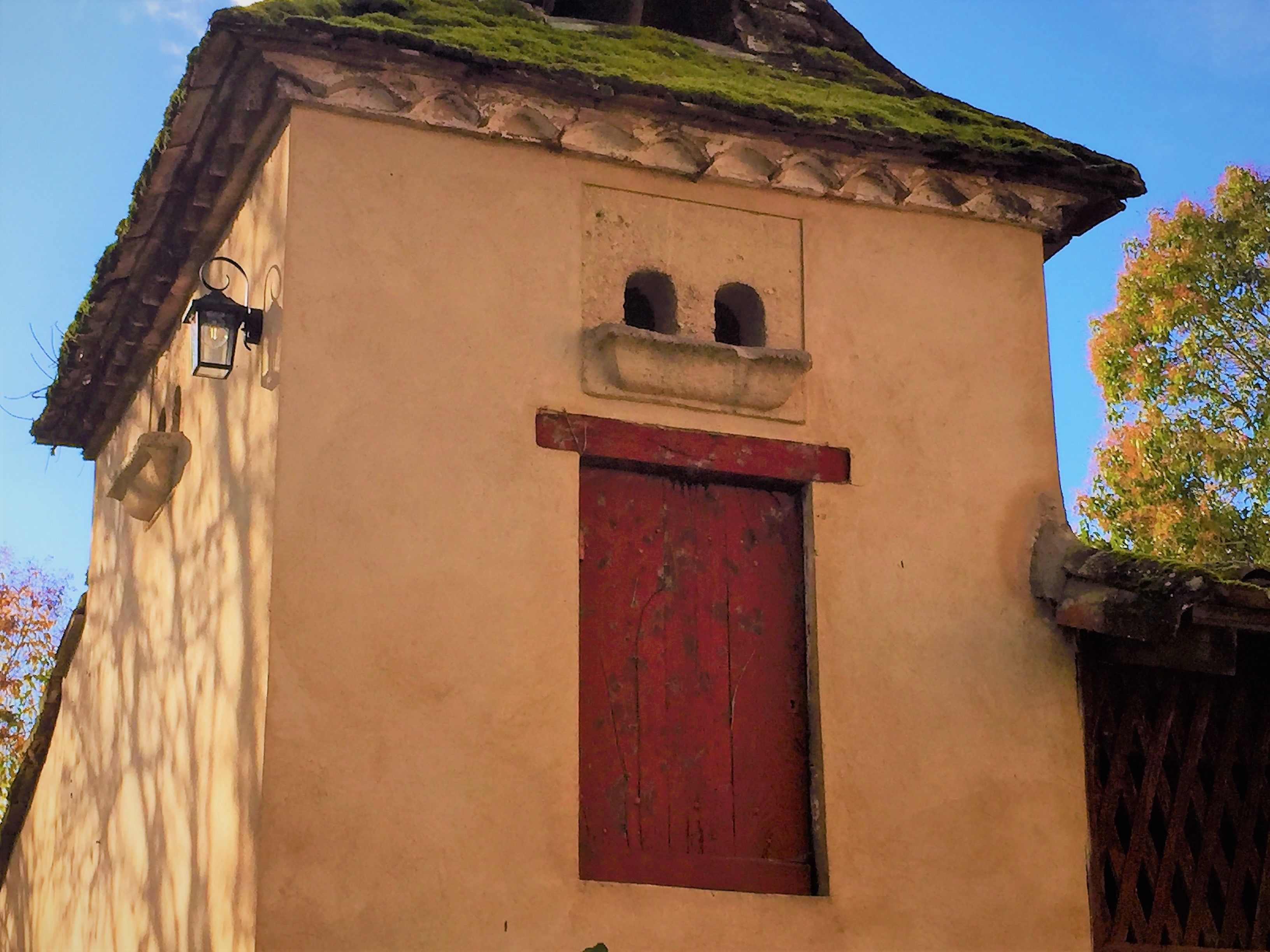 A small building with a red door and a window with two small openings.