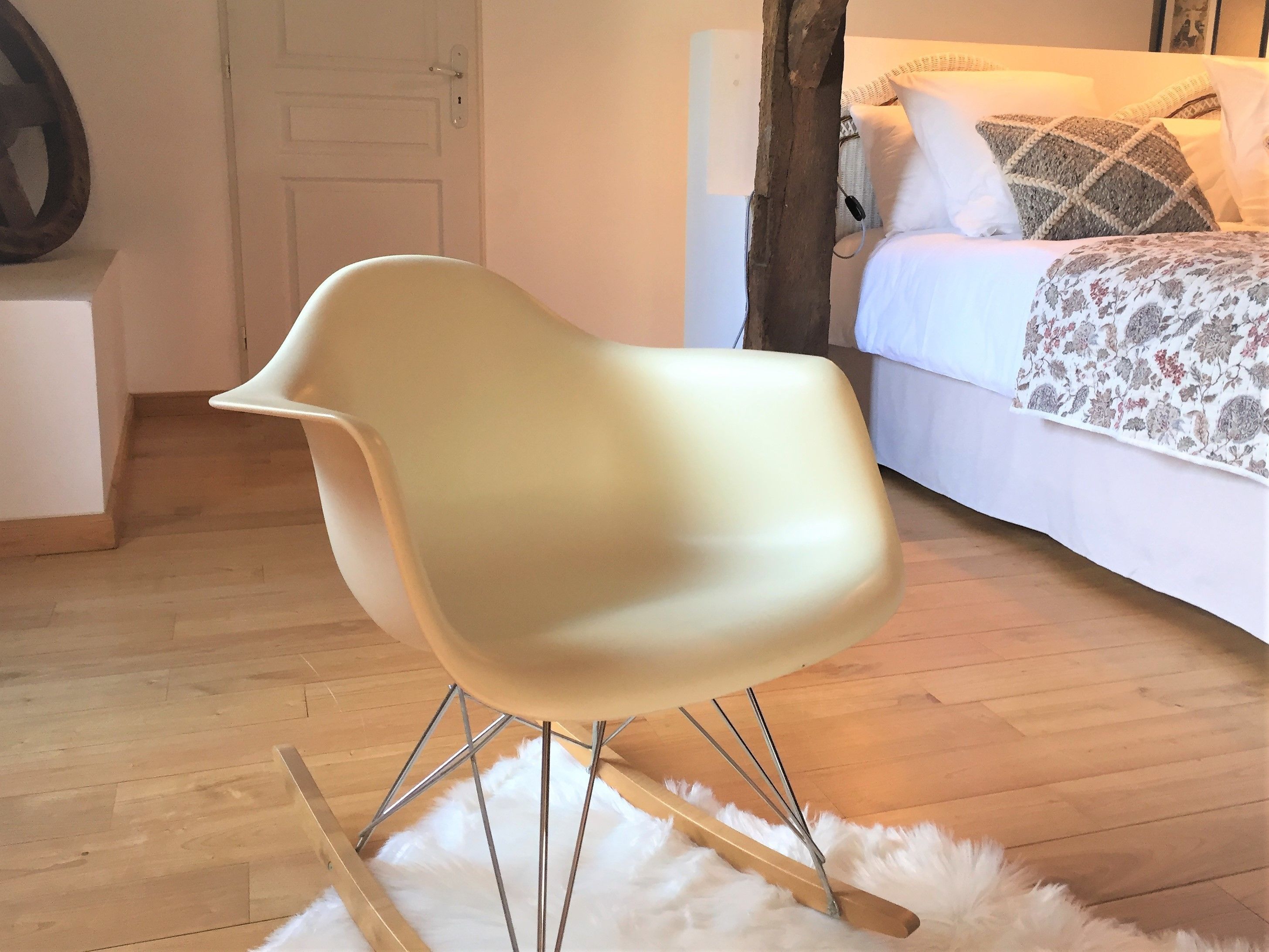 Una habitación moderna con una silla blanca de diseño y patas metálicas, suelo de madera y una alfombra blanca y mullida.