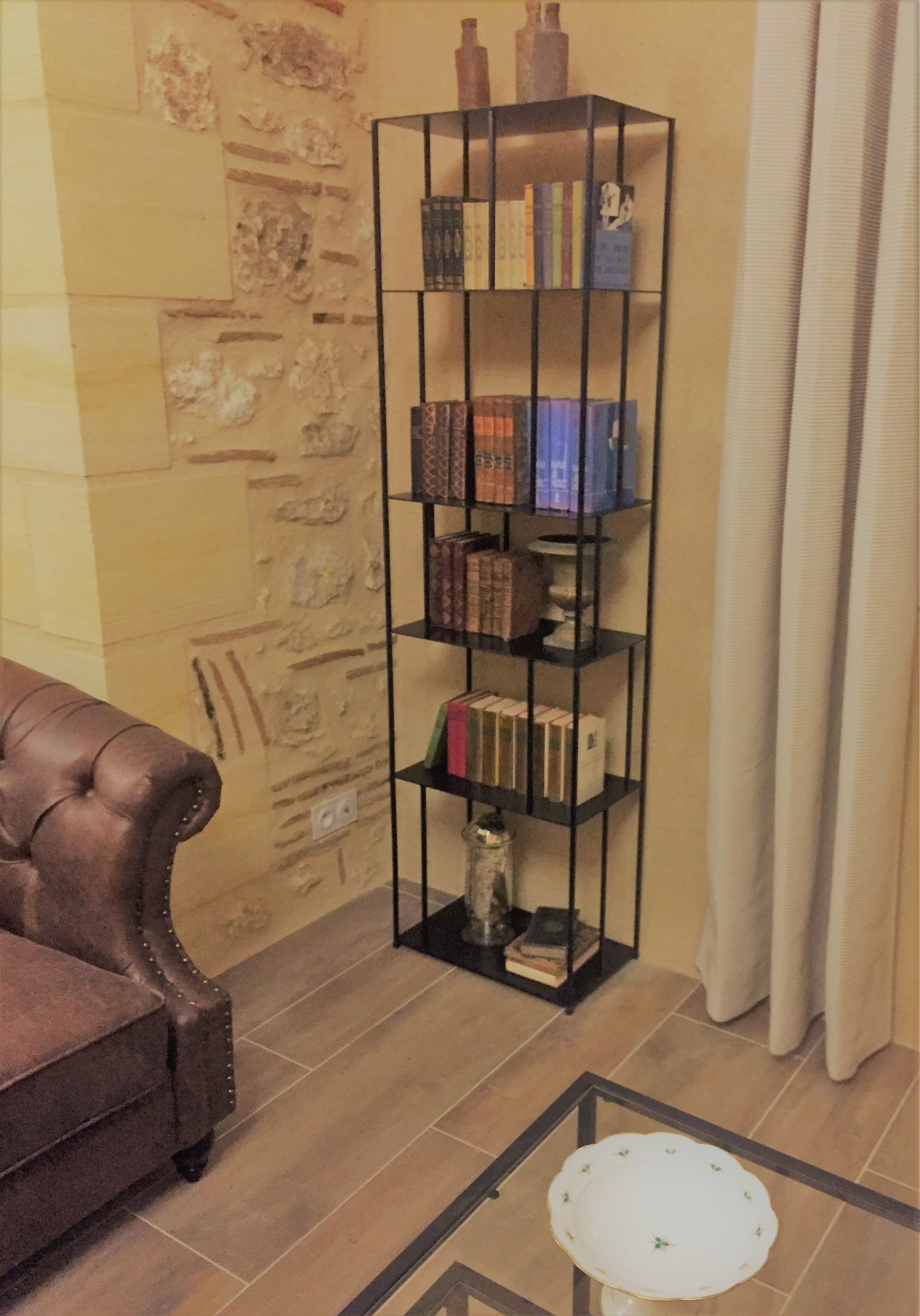A room with a leather sofa, a tall bookshelf, and a small table with a white plate.