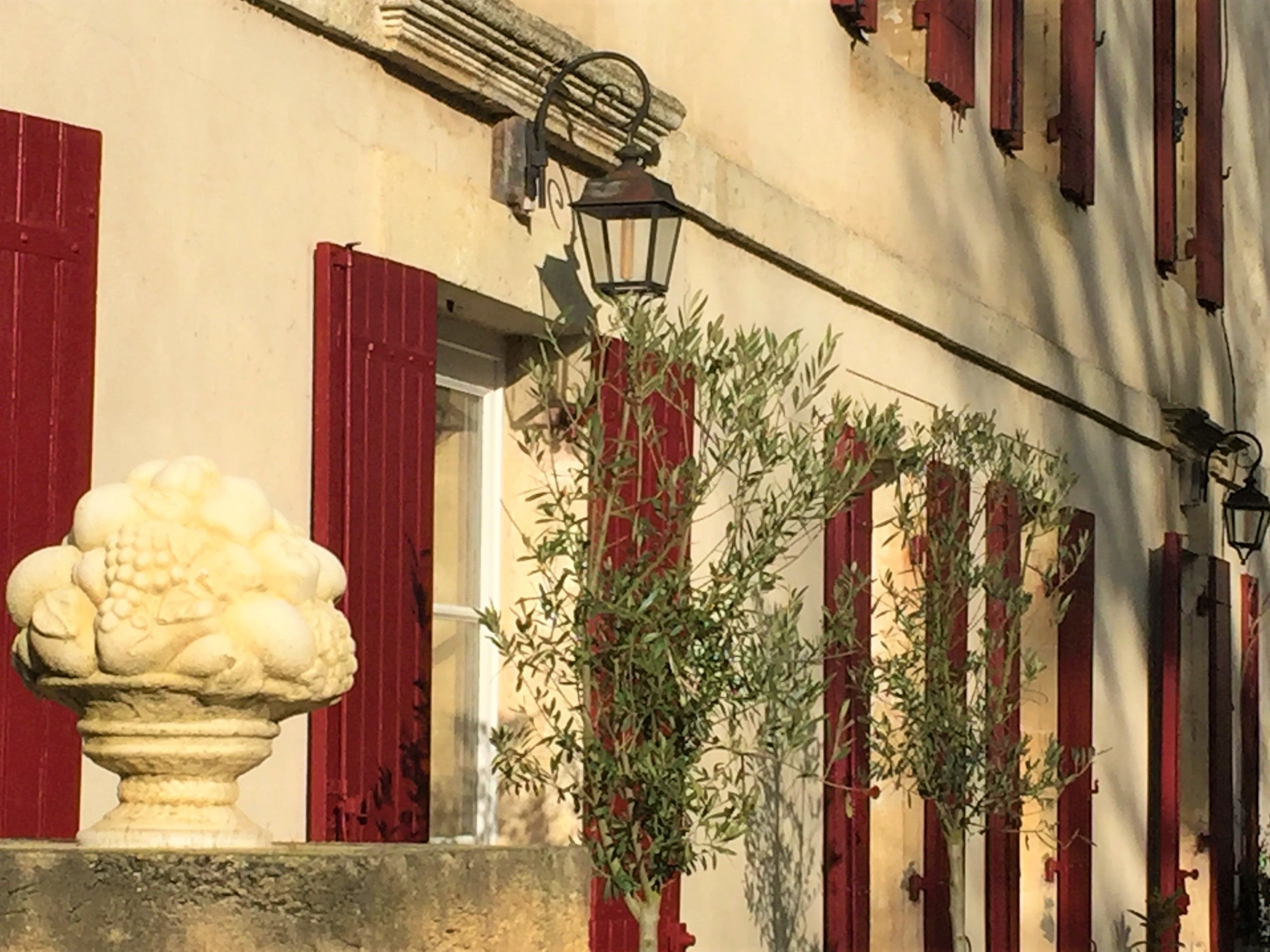 Un bâtiment avec des volets rouges, un piédestal en pierre orné de motifs floraux et un lampadaire.