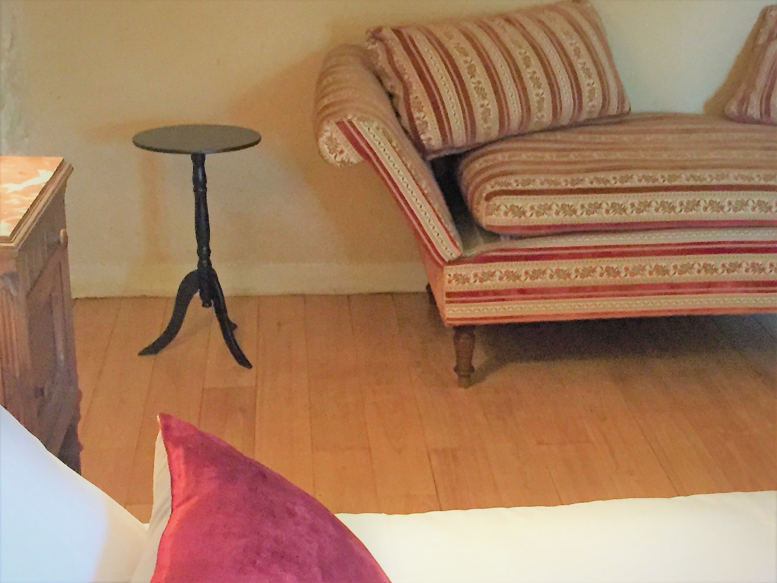 A room with a wooden floor, a striped sofa, a small round table, and a wooden cabinet.