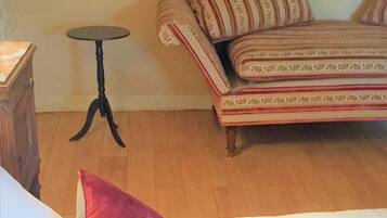 A room with a wooden floor, a striped sofa, a small round table, and a wooden cabinet.