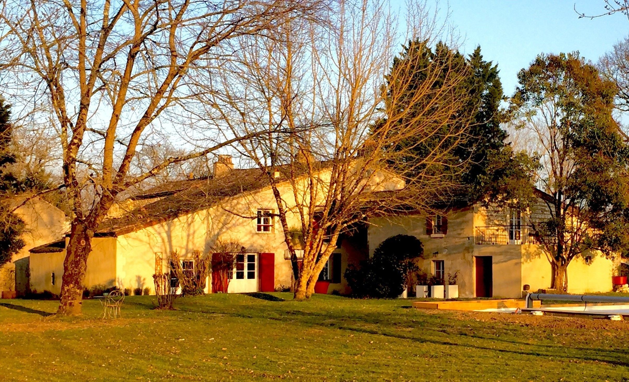 A traditional stone building with a red door, surrounded by trees and a grassy lawn.