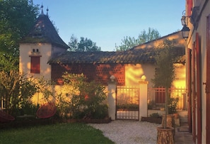 Un patio con un edificio tradicional, una entrada con reja y un pequeño jardín.
