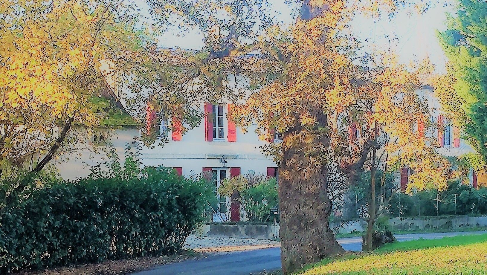 Un edificio de dos pisos con puerta roja y ventanas, rodeado de árboles con hojas amarillas.