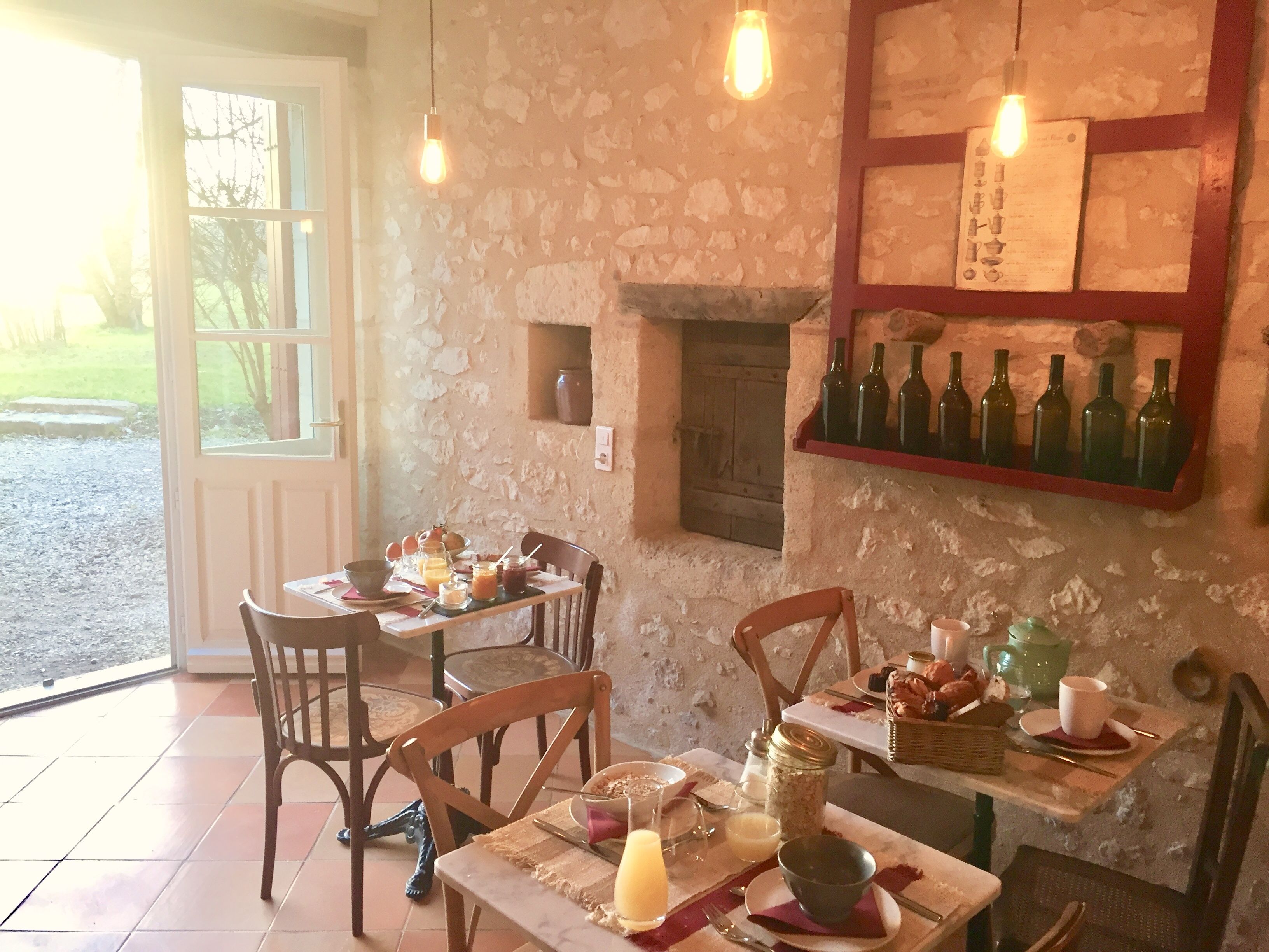 A rustic dining area with a stone wall, wooden chairs, a table set with breakfast, and a wine rack.