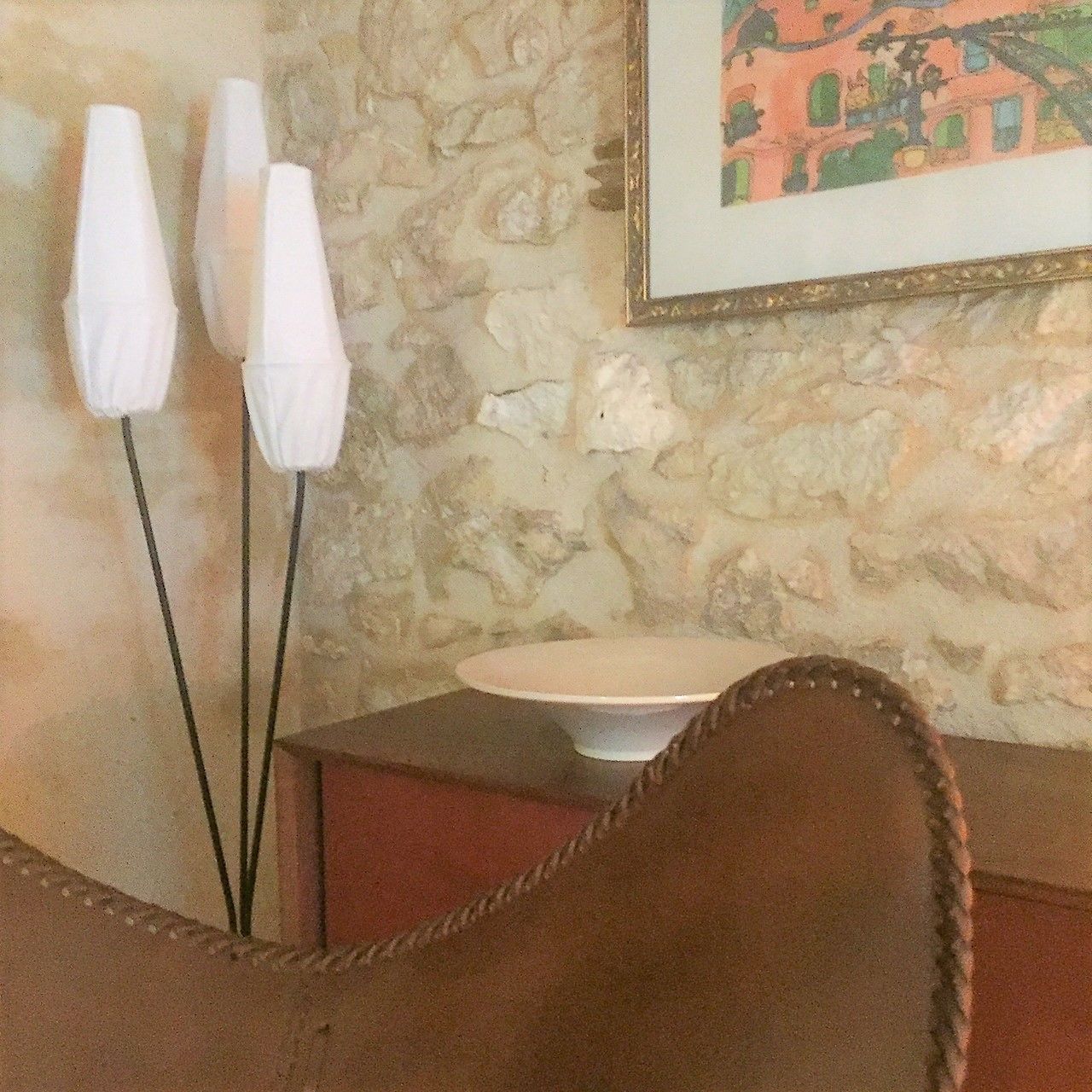 Un muro de piedra con un cuadro enmarcado, una silla marrón y una mesa blanca con un plato.