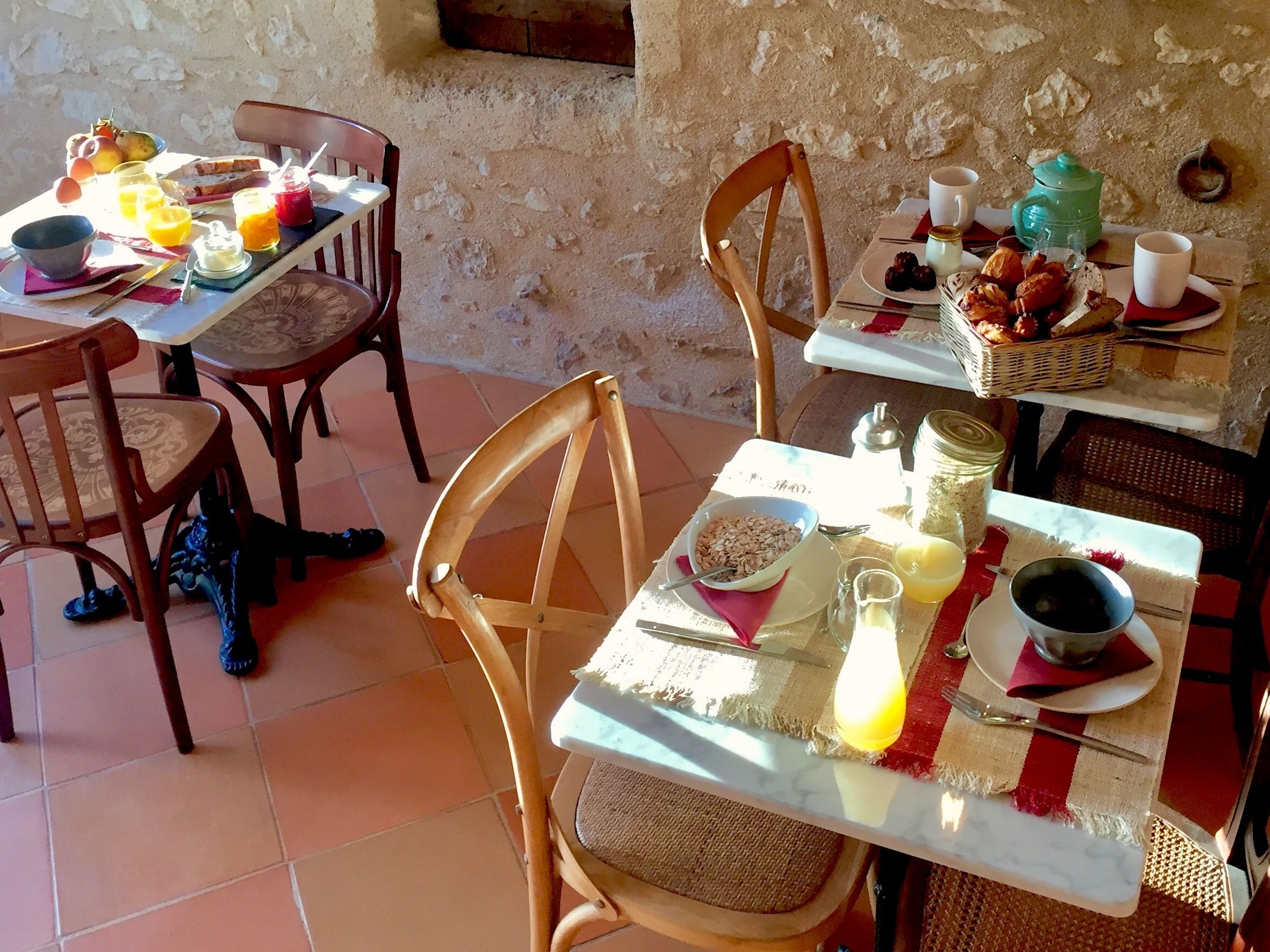 Un espace repas avec des chaises et des tables en bois rustique, où sont proposés des produits pour le petit-déjeuner, comme du pain, des fruits et des boissons.