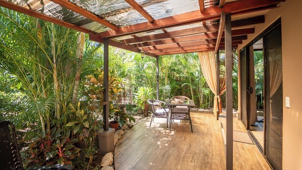 Un patio techado con suelo de madera, rodeado de exuberante vegetación tropical.