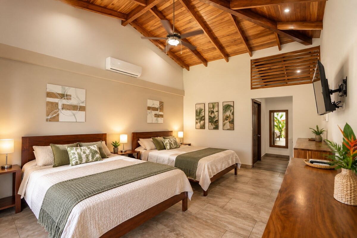 Habitación de hotel con dos camas, vigas de techo de madera, un equipo de aire acondicionado y un televisor montado en la pared.
