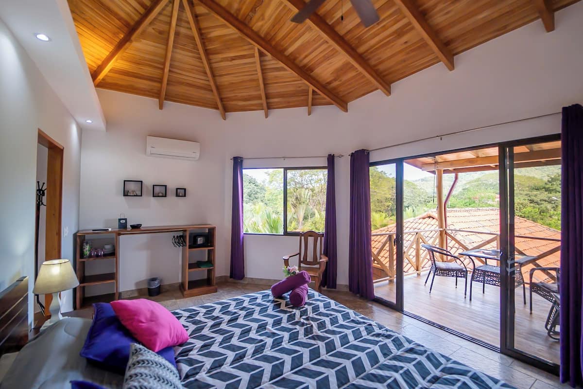 A bedroom with a large bed, a desk, and a view of the outdoor patio.