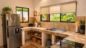 Una cocina con un refrigerador de acero inoxidable, horno empotrado, pileta y ventana con vista a follaje.