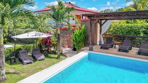 Una piscina con sillas de descanso, una pérgola y una casa con techo rojo.