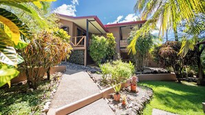Una casa moderna con porche cubierto, rodeada de plantas tropicales y un jardín bien cuidado.