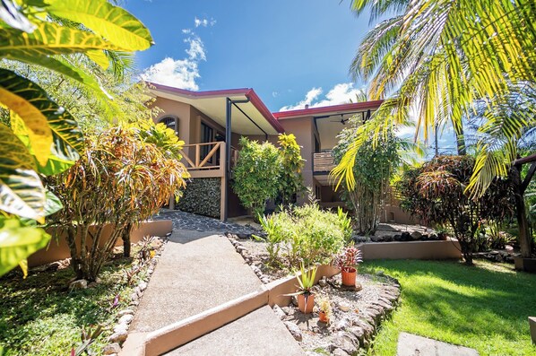 A modern house with a covered porch, surrounded by tropical plants and a well-maintained garden.