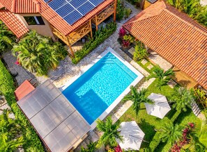 Una piscina rodeada de abundante vegetación y una estructura de techo con tejas.