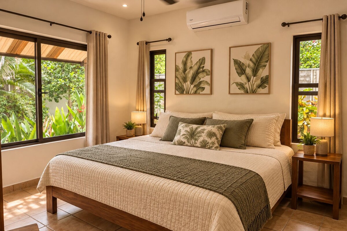 Un dormitorio con una cama grande, dos mesitas de noche, una ventana con cortinas y un aire acondicionado de pared.