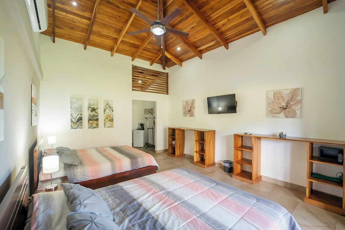 A bedroom with two beds, a ceiling fan, a TV, and a desk with shelves.