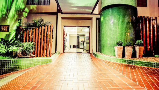 Um corredor com piso ladrilhado, paredes verdes e vasos com plantas.