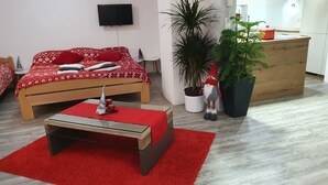 Ein modernes Schlafzimmer mit einem hölzernen Bett, einem kleinen Nachttisch, einem roten Teppich, einer Topfpflanze und einer hölzernen Kommode.