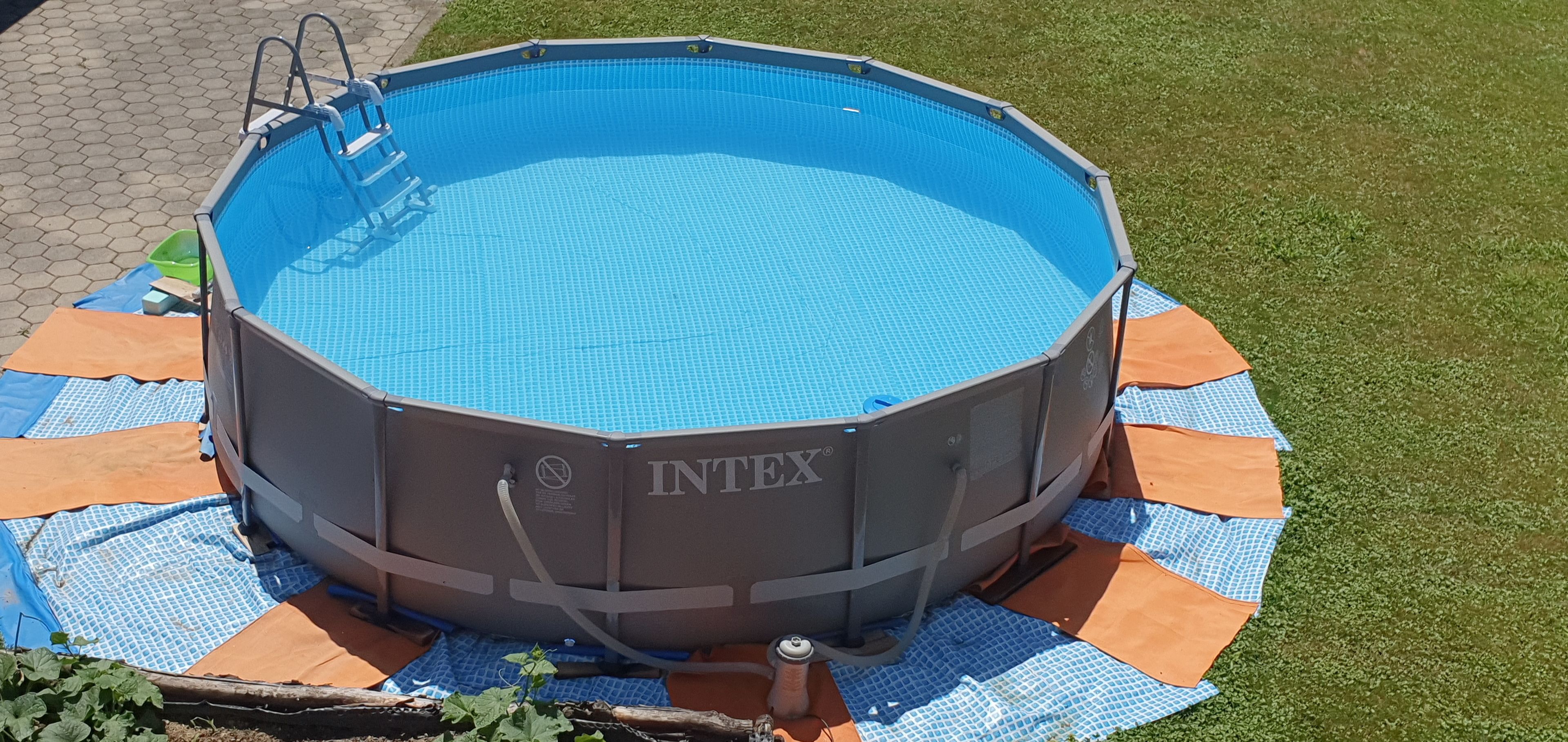 Una piscina hinchable INTEX con una escalera, rodeada por un lona azul y naranja sobre un césped.