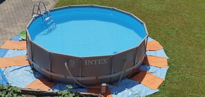 An above-ground INTEX swimming pool with a ladder, surrounded by a blue and orange tarp on a grassy lawn. - Apartments Akacijev Izvir (Miklavž na Dravskem Polju)