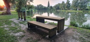 A wooden bench and table by a calm lake with trees and a sunset in the background. - Apartments Akacijev Izvir (Miklavž na Dravskem Polju)