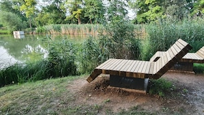 Zwei Holzbänke an einem Teich, umgeben von Grün.