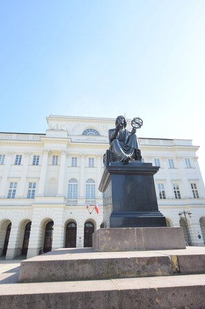 A statue in front of a building with classical architecture, featuring columns and a central dome.