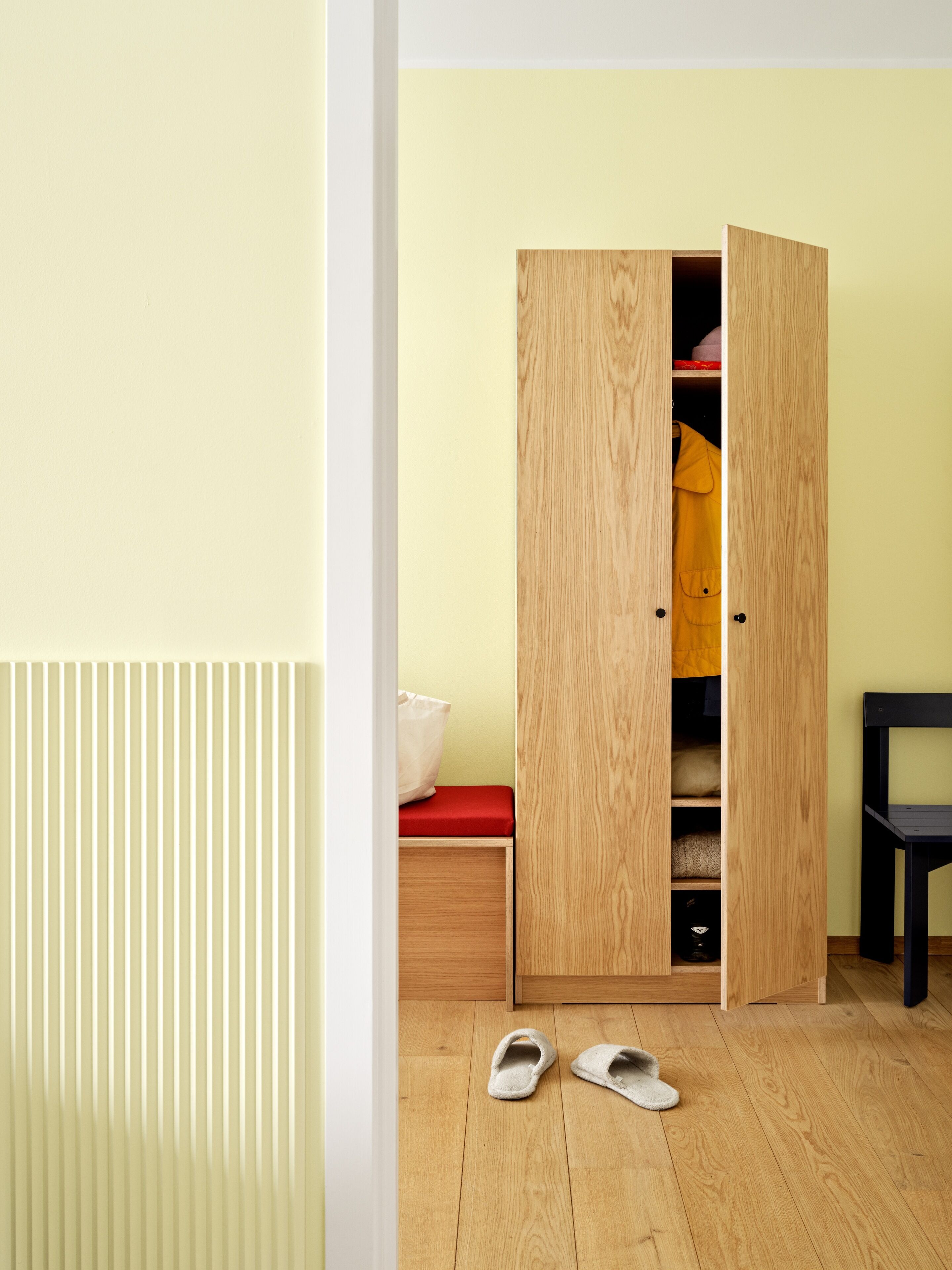 Een kamer met een houten garderobe, een bankje en een paar slippers op de vloer.