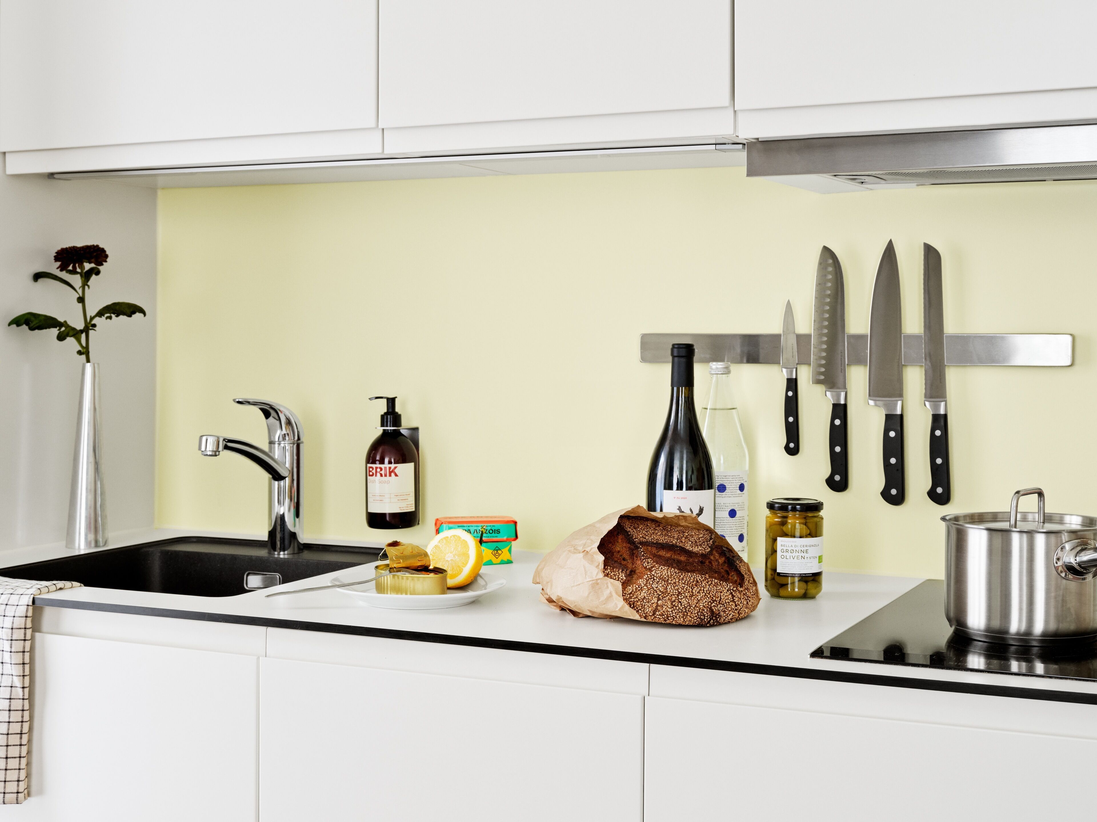 A kitchen with a sink, faucet, and various items like a loaf of bread, a bottle, and a jar.