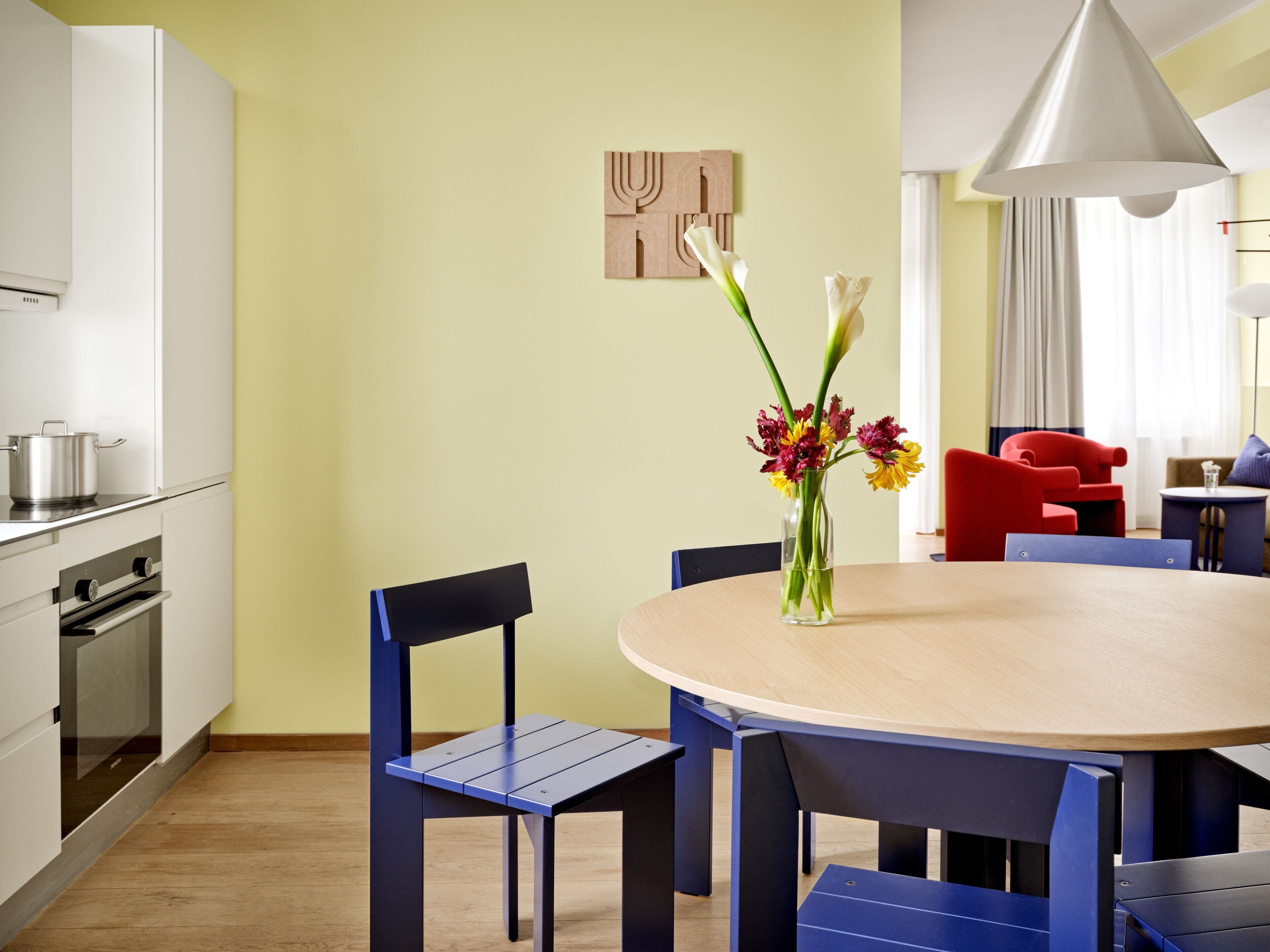 Una cocina moderna con armarios blancos, una estufa y un comedor con una mesa redonda y sillas azules.