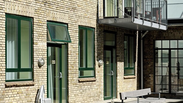 A building with green-framed windows and doors, numbered 23 and 24, and a bench with a yellow towel. - BRIK Apartment Hotel (Copenhagen)