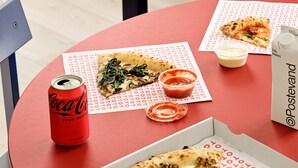 A table with a pizza box, a can of Coca-Cola, a small container of sauce, and a bottle of water. - BRIK Apartment Hotel (Copenhagen)