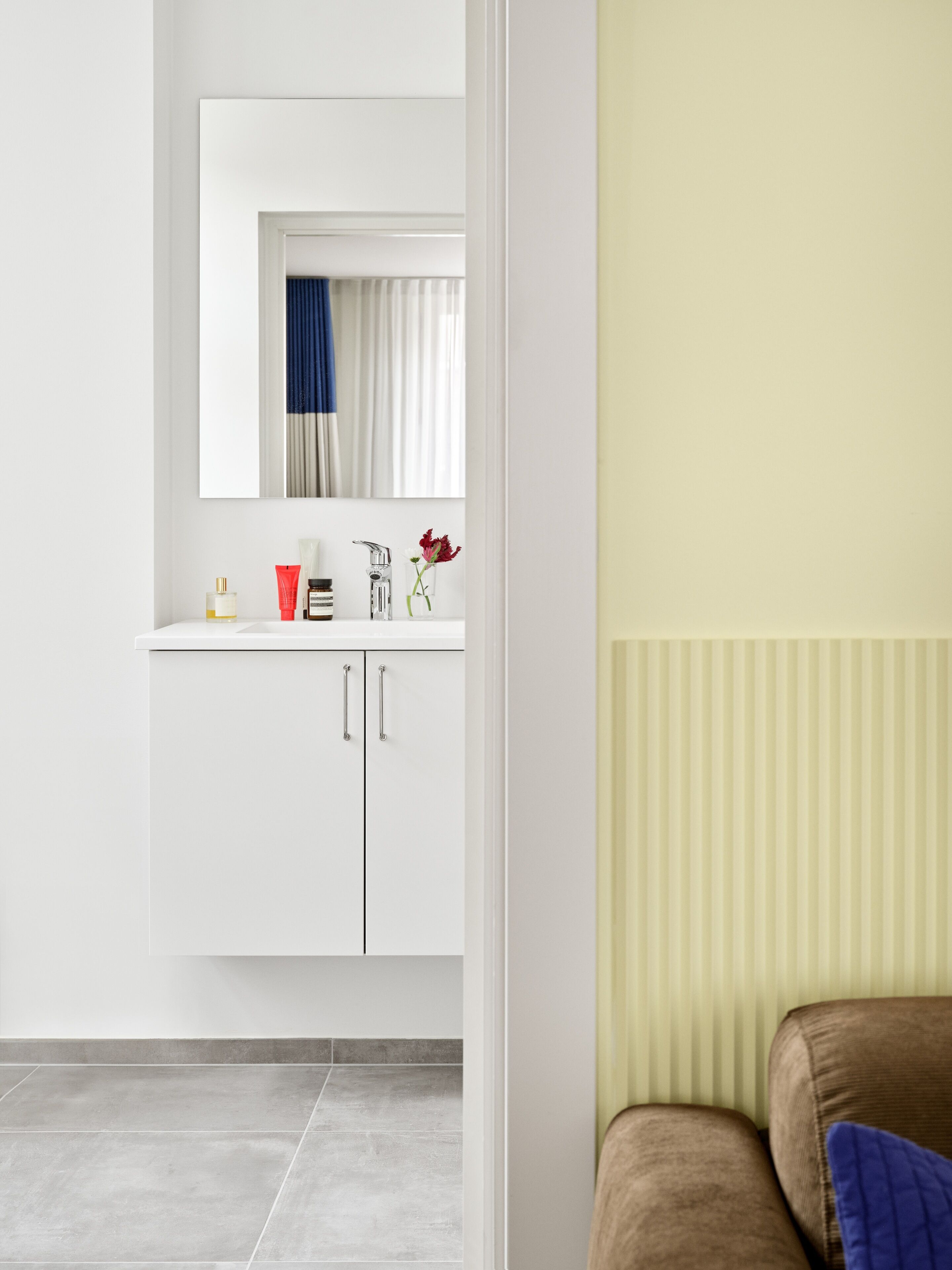 Ein modernes Badezimmer mit einem weißen Waschtisch, einem Spiegel und einem Fenster mit Vorhängen.