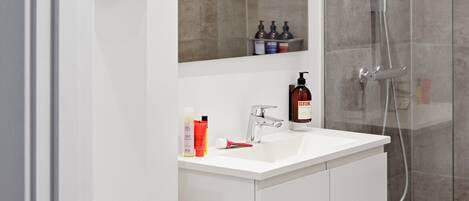 A modern bathroom with a glass shower enclosure, a white vanity with a mirror, and a shelf with toiletries.