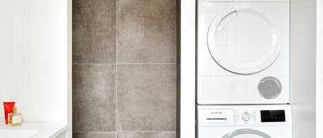 Une petite buanderie équipée d’un lave-linge et d’un sèche-linge Siemens, d’un évier blanc et d’un sol carrelé.