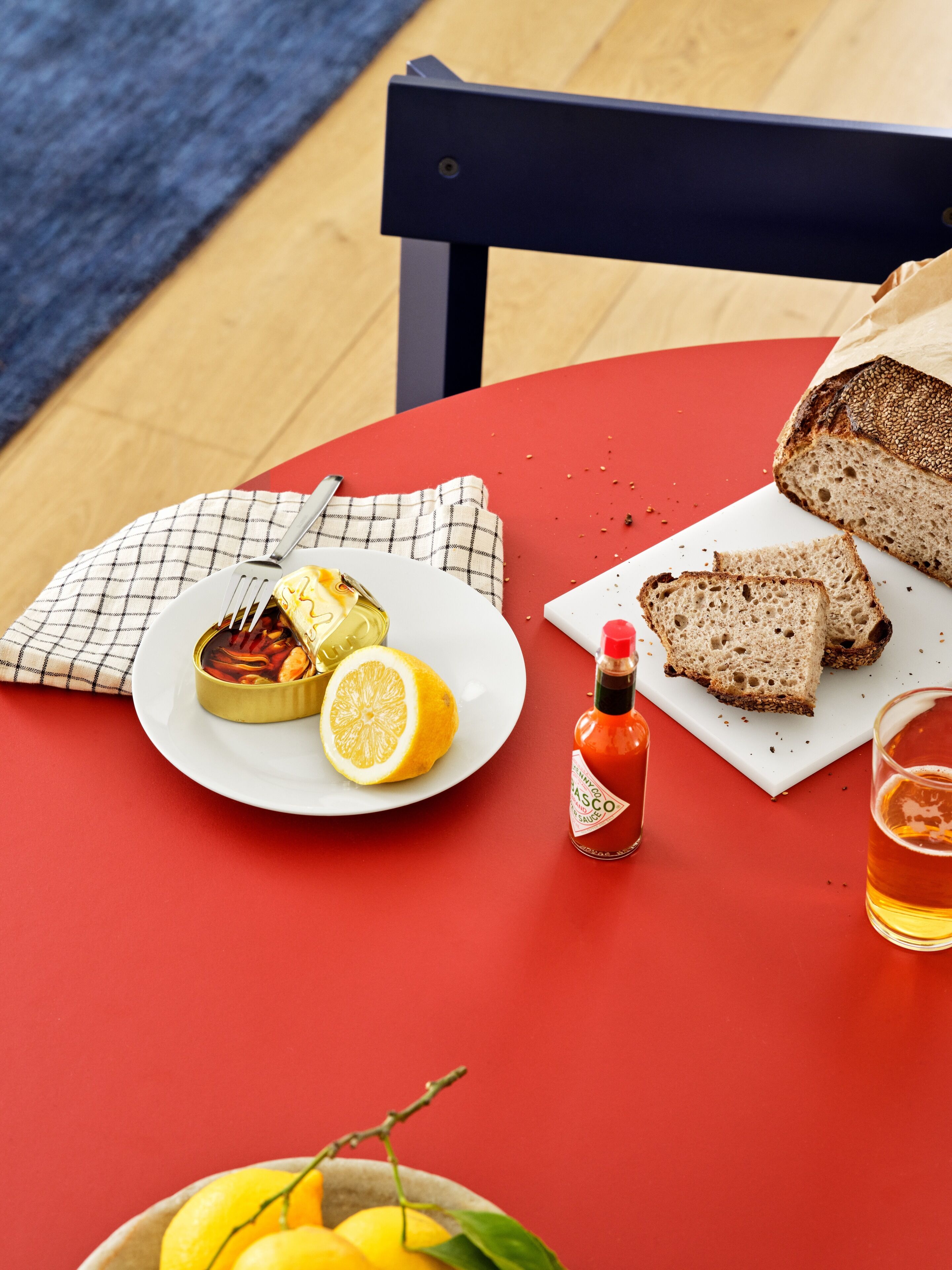 Une table recouverte d’une nappe rouge, une assiette avec un citron et une boîte de sauce, des tranches de pain et une bouteille de sauce.