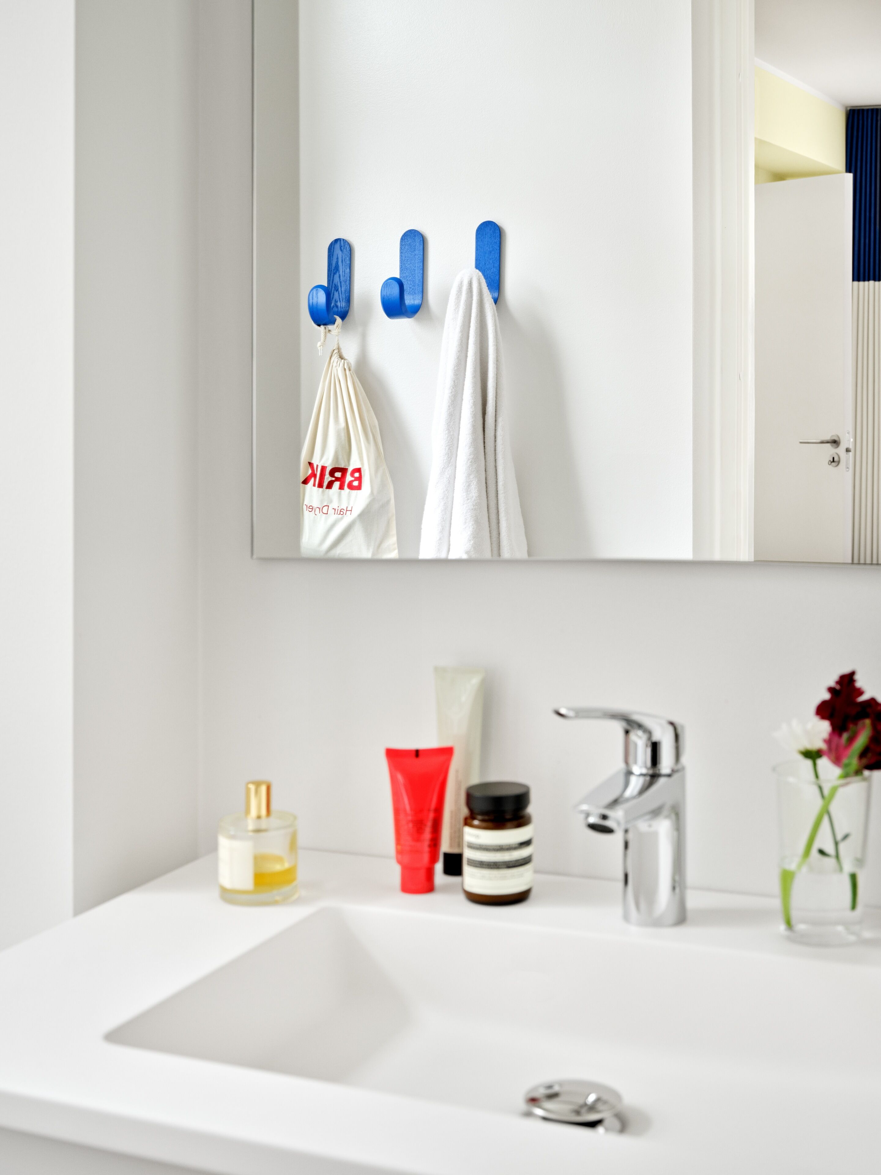 A bathroom with a white sink, a mirror, and toiletries including a bottle of lotion, a red tube, and a jar of cream.