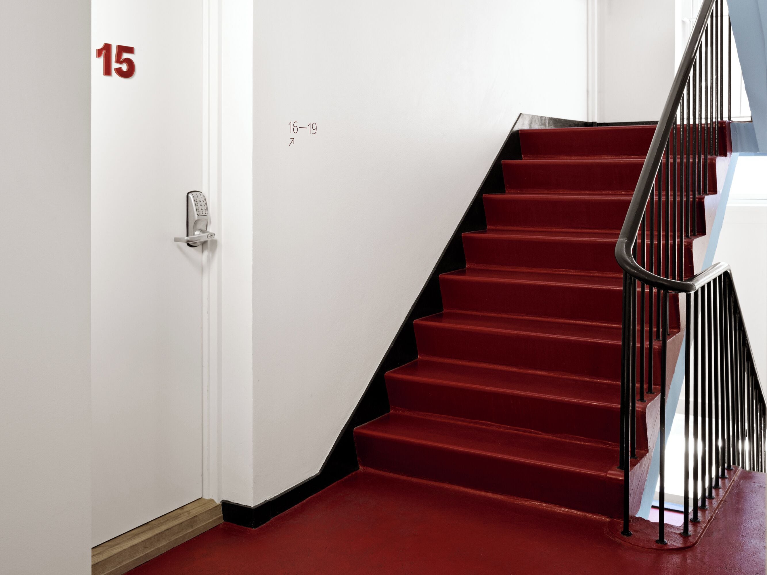 A staircase with red steps and a black railing, leading to a landing with a door marked '15'.