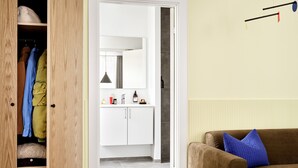 A room with a wooden wardrobe, a brown sofa with a blue pillow, and a white bathroom visible through an open door. - BRIK Apartment Hotel (Copenhagen)