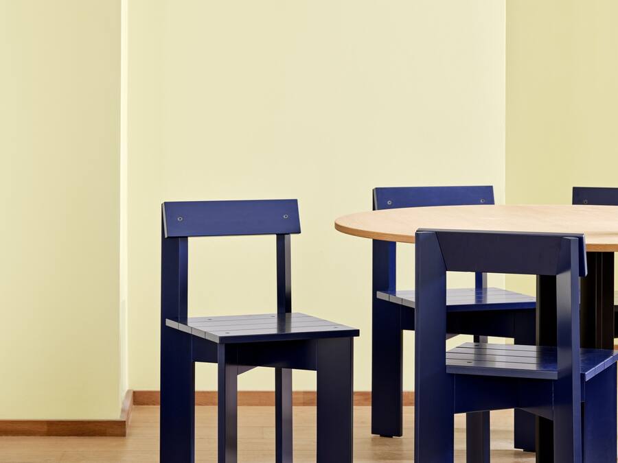 Un coin repas avec une table en bois et des chaises bleues, un luminaire suspendu et un objet rouge au premier plan.