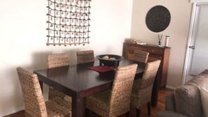 A dining area with a dark wooden table, six woven chairs, a red placemat, a black bowl, and a decorative wall piece.