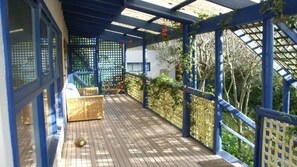 Een overdekt houten terras met blauwe leuningen en een lattenwand.