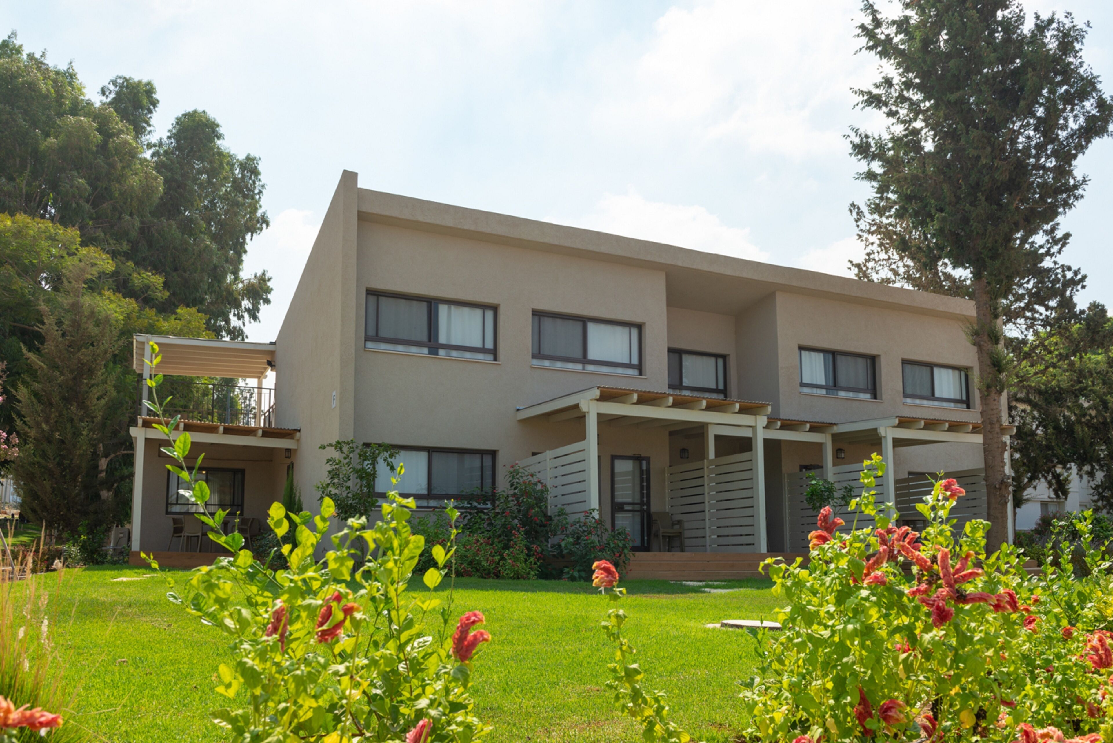 A modern two-story house with a flat roof, large windows, and a covered patio area.