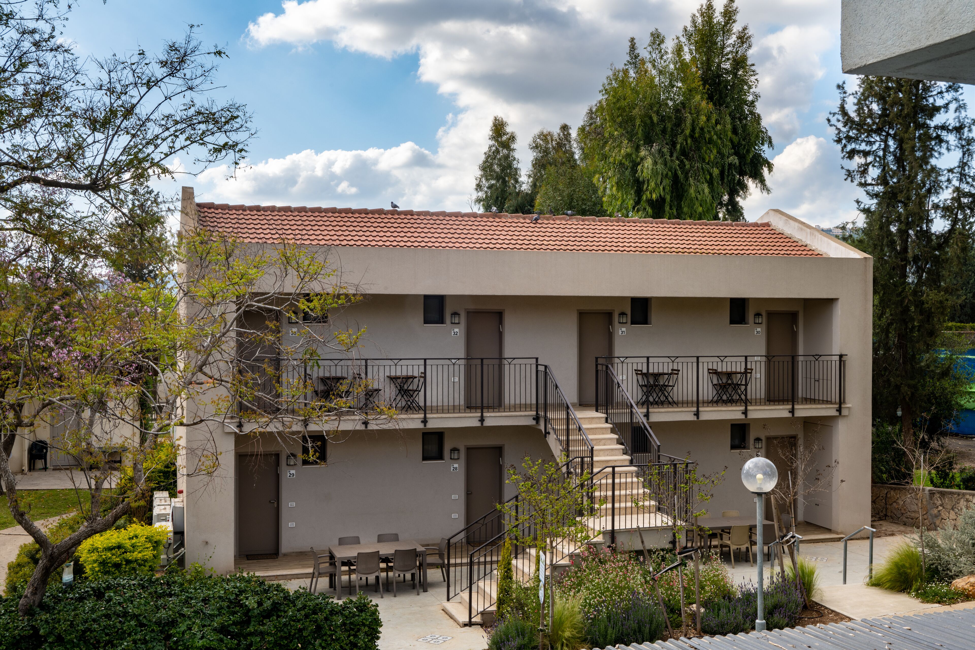 A two-story building with a balcony on the upper floor, outdoor seating, and a staircase leading to the entrance.