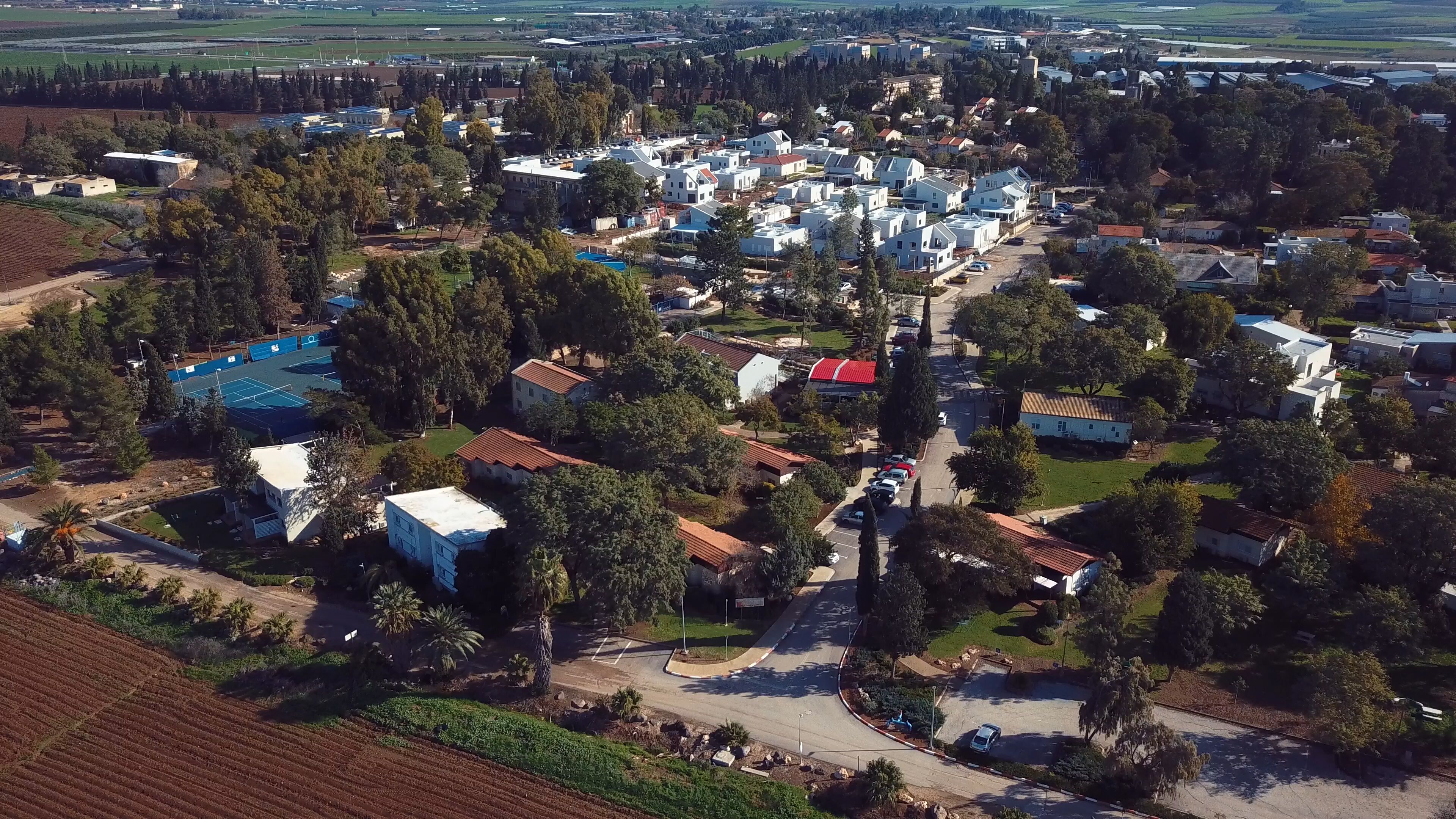 An aerial view of a residential area with houses, a tennis court, and surrounding greenery.